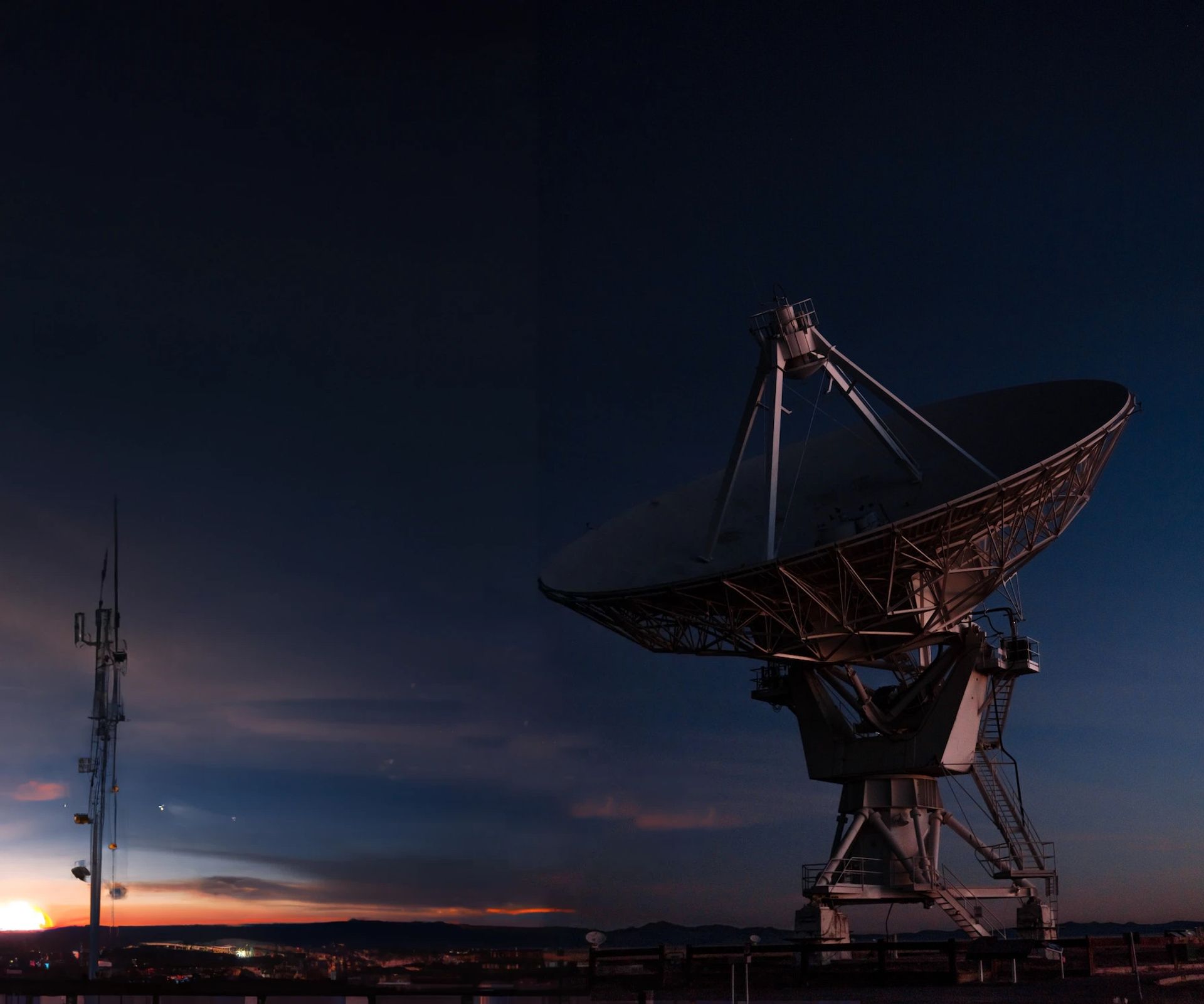 Background image for Vue js developer, a satallite dish points towards space with a deep blue evening sky and orange sunset in the background
